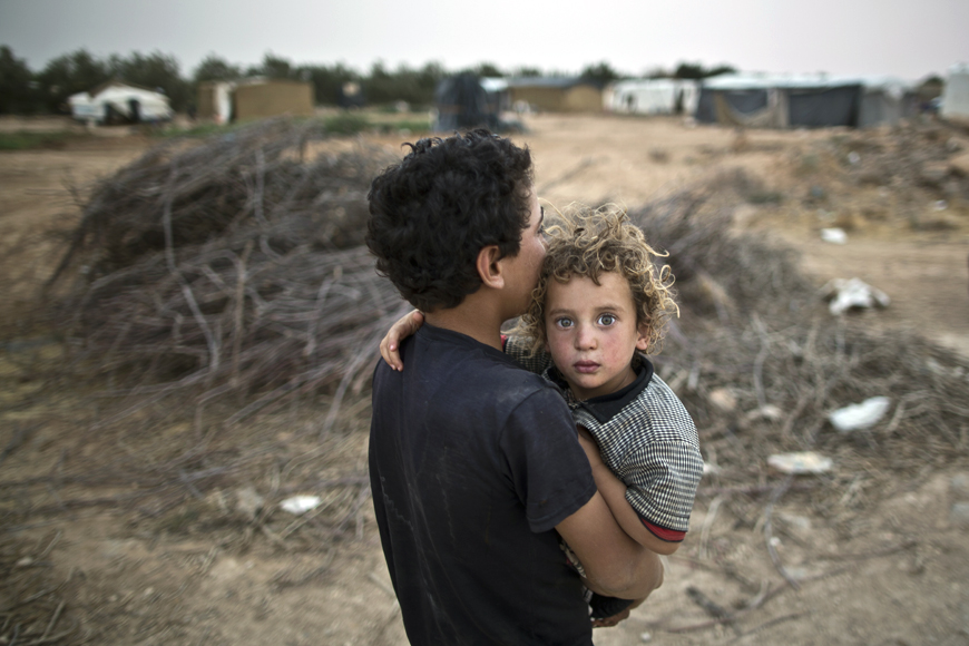 In this photo taken last Tuesday, a Syrian refugee boy carries his younger brother back to their tent at a makeshift  settlement near the Syrian border on the outskirts of Mafraq, some 80km northeast of Amman (AP photo by Muhammed Muheisen)